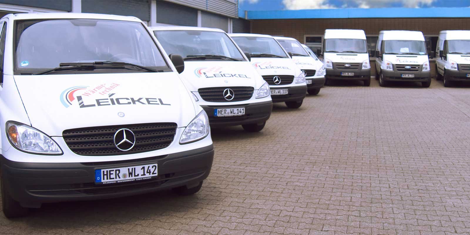 Eine Reihe von weißen Lieferwagen mit dem Logo von Leickel steht auf einem gepflasterten Parkplatz unter einem bewölkten Himmel.
